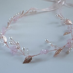 May include: A delicate floral headband featuring a rose gold wire base adorned with faux pearls, pink beads, and metallic leaves. A light pink ribbon is attached for tying. This elegant headpiece is suitable for weddings or special occasions.
