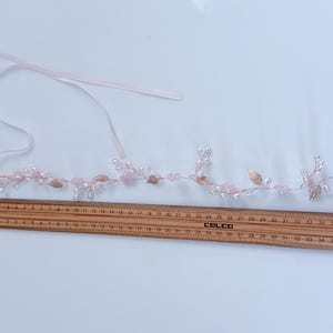 May include: A delicate, pink floral hair accessory with pearl-like beads, rose-colored crystals, and gold-colored leaves. A wooden ruler shows the accessory is approximately 15 inches long. Includes a pink ribbon for tying.