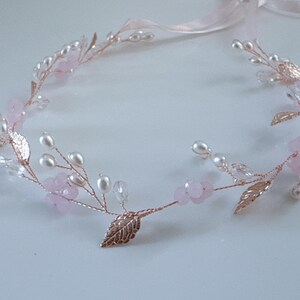 May include: A delicate floral headband with a rose gold wire base. The design features faux pearls, pink flower accents, and metallic gold leaves. A pale pink ribbon is attached for tying.