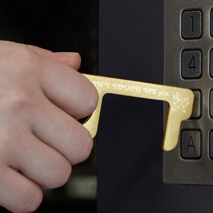 May include: A gold-colored touch tool with the text "Don't Touch Me Please" is being used to press a button on a keypad. The keypad has numbers 1 through 9, and letters A, O, and B.