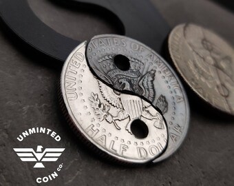 May include: A silver half dollar coin with a yin yang design cut into it. The coin is on a dark gray surface. The coin says "United States of America" and "Half Dollar".