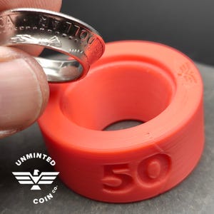 May include: A silver coin ring being placed into a red plastic ring sizer with the text "Unminted Coin Co." and the number "50" printed on the side.