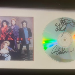 Può includere: Stampa incorniciata della copertina dell'album Heart e CD autografato. La copertina dell'album presenta un gruppo di cinque persone in abiti colorati. Il CD è firmato con inchiostro nero. La cornice è nera con un passe-partout bianco.
