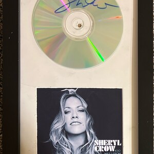 May include: Framed CD and album art featuring Sheryl Crow. The CD is signed in blue ink. The album art is a black and white photo of Sheryl Crow with the album title "100 Miles From Memphis".