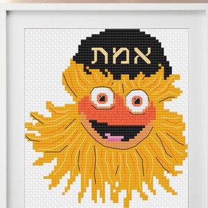 May include: Cross stitch pattern of a yellow and orange Sesame Street character wearing a black yarmulke with the Hebrew word "Amah" written on it.