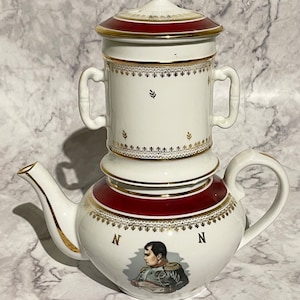 May include: White porcelain teapot with a red and gold trim. The teapot features a portrait of Napoleon Bonaparte and the letter "N" on either side. The teapot has a removable top with a lid.