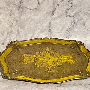 May include: A decorative tray with a gold and yellow finish. The tray has a scalloped edge and a floral design in the centre.
