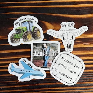 May include: Five stickers with different designs. A green tractor sticker with the text "Big Green Tractor". A skull sticker with the text "Try That In a small town". A sticker with a blue airplane and the text "Fly Over States". A sticker with the text "Mommas let your boys be country" surrounded by barbed wire. A sticker with a photo of Jason Aldean and the text "My Kinda Party Jason Aldean".