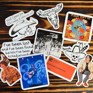May include: A collection of 10 stickers featuring various designs, including a skull with a cowboy hat, a skull with a feather, a skeleton playing a guitar, and a man with a guitar. The stickers are printed on white paper with black ink. The text on the stickers includes "Well I guess you didn't mean it when you said that you love me", "I've been lost and I've been found Lately I've been kicked around", "So please don't go", "Break", "Life Lessons", "Fuck around and fall in love", "PLEASE DON'T GO", and "my".