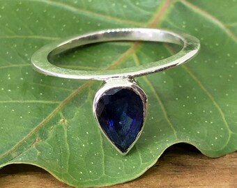 May include: A silver ring with a teardrop-shaped blue gemstone. The ring is on a green leaf.