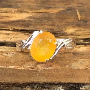 Puede incluir: Un anillo de plata con una piedra preciosa amarilla engastada en una banda retorcida.
