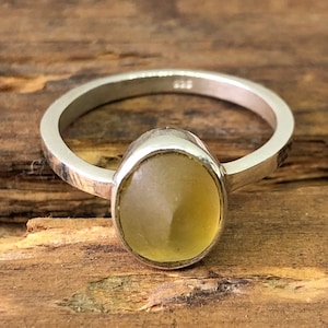 May include: A silver ring with a yellow oval gemstone. The ring is on a wooden surface.