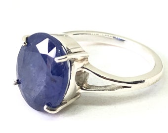 Op de afbeelding: Een zilveren ring met een grote, ovaalvormige, diepblauwe edelsteen. De edelsteen is gezet in een eenvoudige zilveren band. De ring wordt getoond tegen een effen witte achtergrond, waardoor de kleur en het ontwerp worden benadrukt.