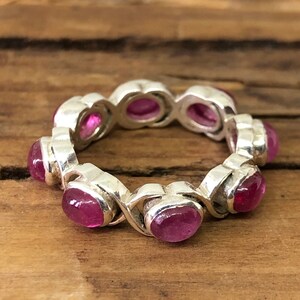 Könnte beinhalten: Ein silberner Ring mit einer Reihe von ovalen rosafarbenen Edelsteinen. Der Ring liegt auf einer Holzoberfläche.