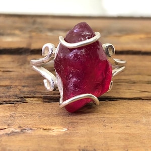 May include: A silver ring featuring a large, deep pink, irregularly shaped gemstone set in a delicate, twisted wire design.