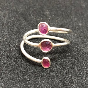 以下が含まれることがあります： 螺旋状のデザインに3つのピンクの宝石がセットされたシルバーリングです。