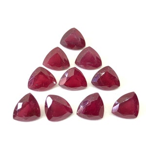 Può includere: Dieci pietre preziose rosse triangolari, note anche come rubini, sono disposte a forma di triangolo su uno sfondo bianco.