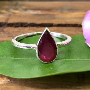 Puede incluir: Un anillo de plata con una piedra preciosa de rubí en forma de lágrima.