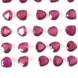 Op de afbeelding: Vijfentwintig losse, gefacetteerde, hartvormige robijn edelstenen. De robijnen zijn diep roze van kleur en zijn gerangschikt in vijf rijen van vijf.