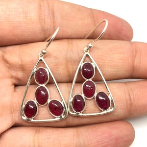 Puede incluir: Un par de pendientes de plata con un diseño triangular y tres piedras preciosas rojas en cada pendiente.