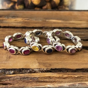 Könnte beinhalten: Drei silberne Ringe mit bunten Edelsteinen. Die Ringe sind übereinander gestapelt. Die Edelsteine sind rosa, blau und gelb.