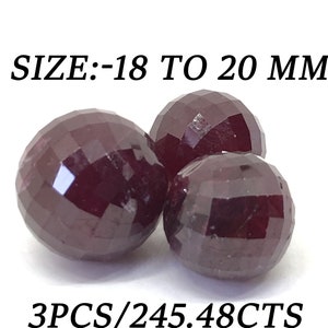 May include: Three dark red faceted gemstone beads, each measuring 18 to 20 mm in diameter. The beads are arranged in a cluster on a white background. The text "SIZE: -18 TO 20 MM" and "3PCS/245.48CTS" is visible below the beads.