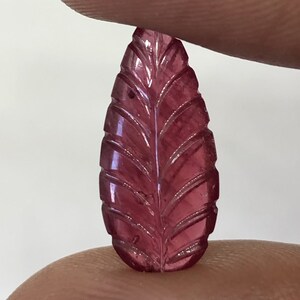 Pode incluir: Uma gema rosa esculpida em forma de folha. A gema é translúcida e tem um design delicado e intrincado.