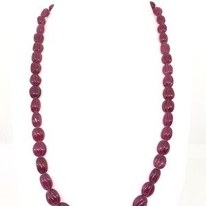 May include: A long necklace made of deep red oval-shaped beads. The beads have a textured surface.