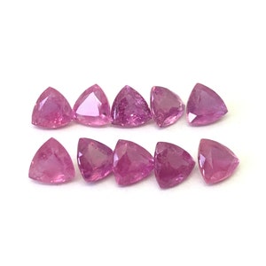 Puede incluir: Diez piedras preciosas triangulares de color rosa, probablemente zafiros, dispuestas en dos filas sobre un fondo blanco.