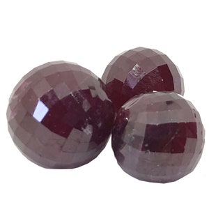 May include: Three dark red faceted gemstone beads. The beads are round and have a smooth, polished finish.