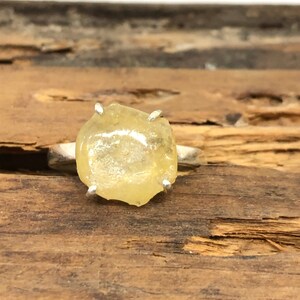 Peut inclure: Une bague en argent avec une grosse pierre précieuse jaune brute sertie sur quatre griffes.