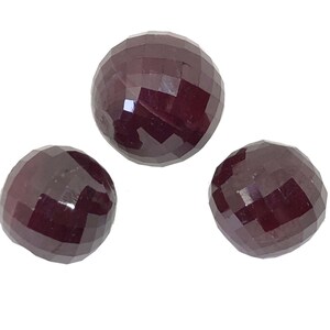 May include: Three round, faceted ruby gemstones. The gemstones are a deep red color and have a polished finish.