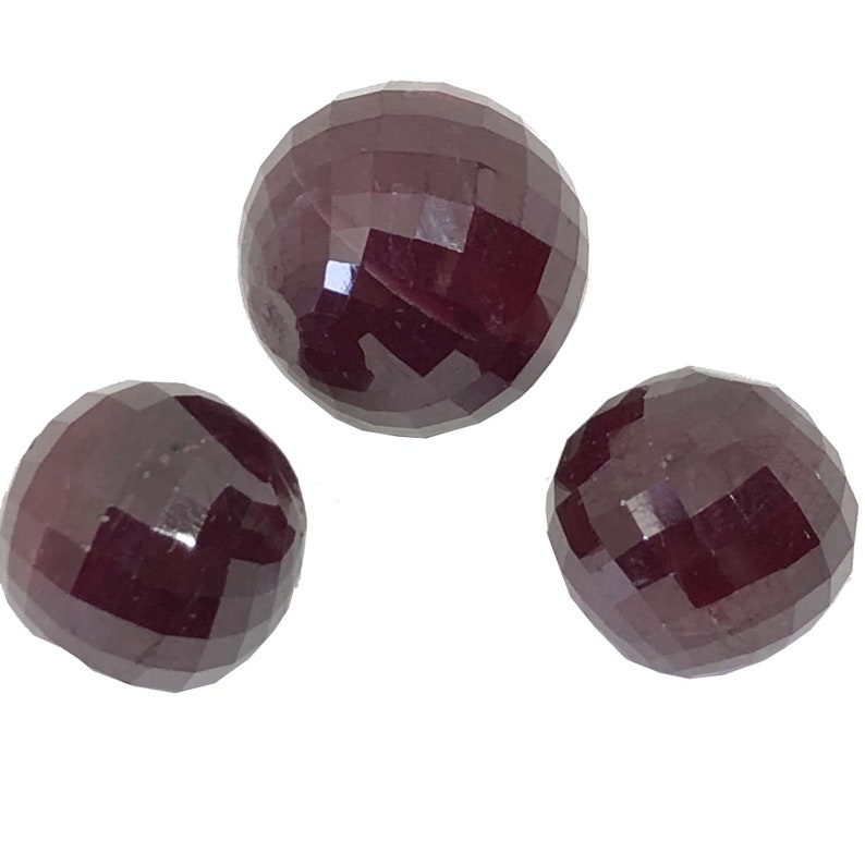 May include: Three round, faceted ruby gemstones. The gemstones are a deep red color and have a polished finish.