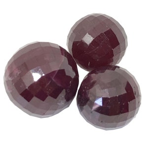 May include: Three round, faceted ruby gemstones. The gemstones are a deep red color and have a high polish.