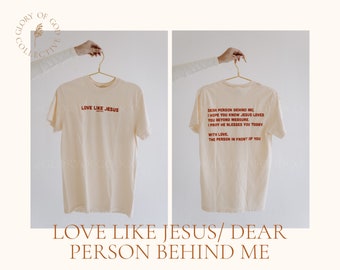 Op de afbeelding: Een crèmekleurig T-shirt met de tekst "Love Like Jesus" op de voorkant en "Dear Person Behind Me, I hope you know Jesus loves you beyond measure. I pray he blesses you today. With love, the person in front of you" op de achterkant.
