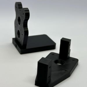 May include: Three black 3D printed plastic pieces for a camera mount. The pieces are designed to be assembled together to create a stable platform for a camera.