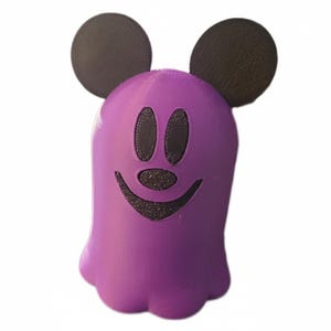 May include: A purple ghost-shaped figurine with black eyes, a smiling mouth, and two black circular ears. The figurine has a smooth texture and is set against a white background. The design is reminiscent of a popular cartoon character.