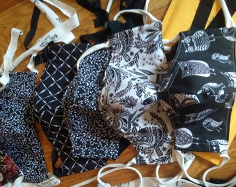 May include: A collection of five black and white fabric face masks with various patterns. The masks are made of cotton and have adjustable ear loops. The patterns include birds, leaves, and geometric designs.