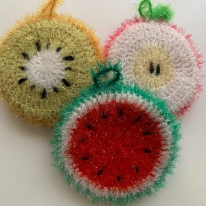 May include: Three crocheted dishcloths shaped like fruit. A green kiwi, a white apple, and a red watermelon.