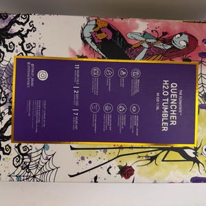 Puede incluir: Una caja morada y dorada con una ilustraci&oacute;n estilizada de Sally de Pesadilla antes de Navidad. La caja contiene un vaso Stanley Quencher H2.0, con texto que indica que mantiene las bebidas fr&iacute;as durante 11 horas y heladas durante 2 d&iacute;as.