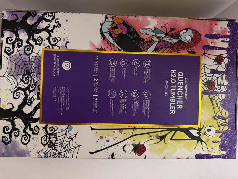 Puede incluir: Una caja morada y dorada con una ilustraci&oacute;n estilizada de Sally de Pesadilla antes de Navidad. La caja contiene un vaso Stanley Quencher H2.0, con texto que indica que mantiene las bebidas fr&iacute;as durante 11 horas y heladas durante 2 d&iacute;as.