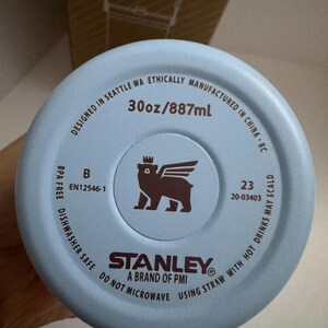 Puede incluir: Base de vaso Stanley azul claro con el texto "30oz/887ml". La base incluye el logotipo de Stanley, un oso con alas y corona, y el texto "BPA FREE DISHWASHER SAFE DO NOT MICROWAVE USING STRAW WITH HOT DRINKS MAY SCALD".