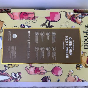 K&ouml;nnte beinhalten: Eine gelbe Box mit Winnie-the-Pooh-Figuren. Die Box enth&auml;lt einen "QUENCHER H2.0 TUMBLER" mit einem Fassungsverm&ouml;gen von 1,18 l. Die Box enth&auml;lt auch Informationen &uuml;ber die Kalt-, Eis- und Hei&szlig;haltezeiten des Tumblers.