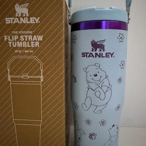 Puede incluir: Un vaso Stanley The Iceflow Flip Straw de color azul claro, 887 ml, con una caja a juego. El vaso presenta un dise&ntilde;o de Winnie the Pooh con detalles florales y de abejas. Tiene un borde y un asa morados.