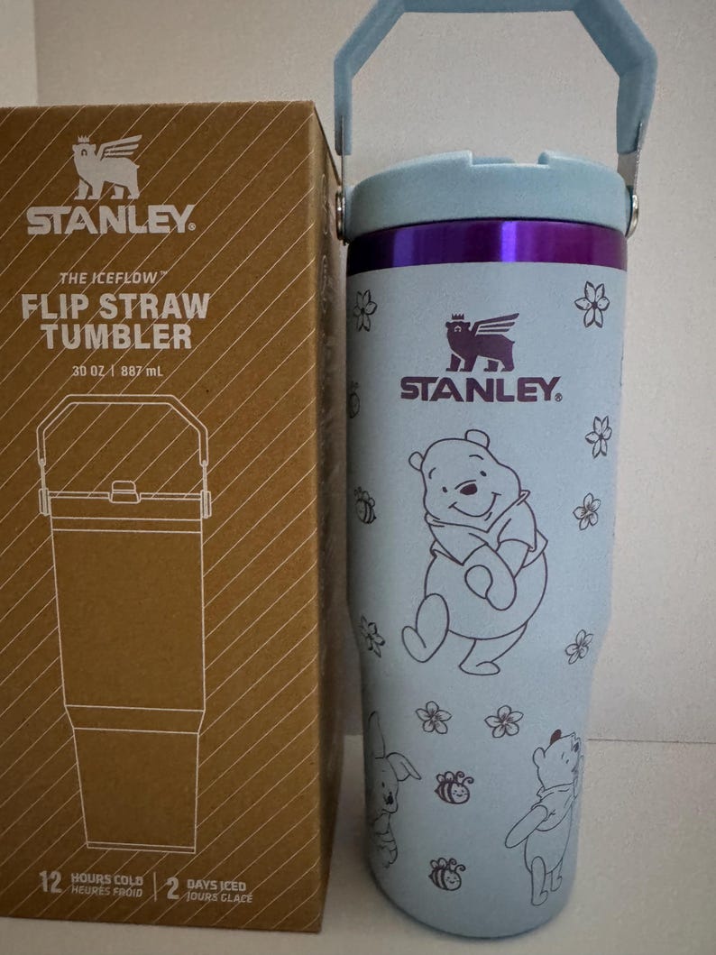 Puede incluir: Un vaso Stanley The Iceflow Flip Straw de color azul claro, 887 ml, con una caja a juego. El vaso presenta un dise&ntilde;o de Winnie the Pooh con detalles florales y de abejas. Tiene un borde y un asa morados.