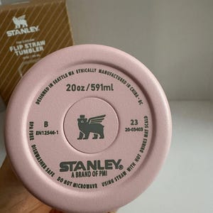 May include: A pink Stanley Flip Straw Tumbler, 20oz/591ml, with the brand logo and text. The bottom of the tumbler is visible, displaying product information and safety instructions. The tumbler is dishwasher safe and BPA free.