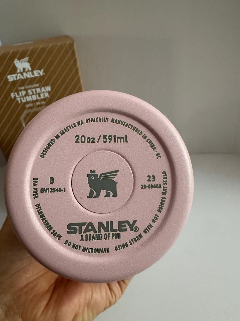 May include: A pink Stanley Flip Straw Tumbler, 20oz/591ml, with the brand logo and text. The bottom of the tumbler is visible, displaying product information and safety instructions. The tumbler is dishwasher safe and BPA free.