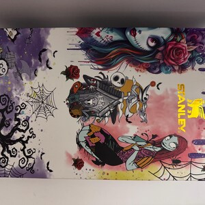 Puede incluir: Una caja rectangular con un dise&ntilde;o colorido con personajes de Pesadilla antes de Navidad. La caja tiene un borde morado y el logotipo de Stanley en dorado. La obra de arte incluye a Jack Skellington, Sally y otros elementos espeluznantes.