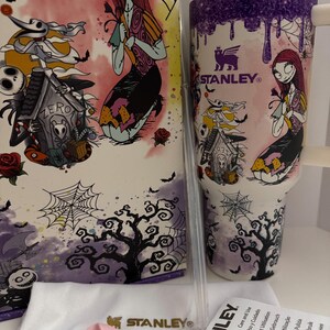 Puede incluir: Un juego de vaso y caja Stanley con Sally de Pesadilla antes de Navidad. El vaso es blanco con un dise&ntilde;o de goteo morado e ilustraciones de personajes. La caja tiene ilustraciones similares, incluyendo a Zero y una casa espeluznante. Los accesorios incluyen un asa rosa y una pajita transparente.