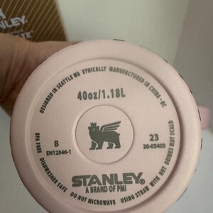 May include: A pink Stanley brand tumbler bottom with the text "40oz/1.18L". The tumbler is dishwasher safe and BPA free. The bottom also features the Stanley logo and a winged bear logo.
